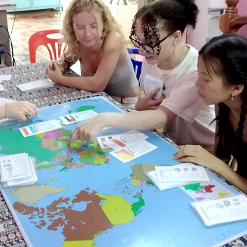 Three young women play a geography game, with a map and cards on the table