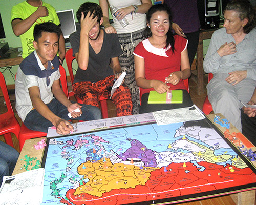Three young Laotians and a visitor sit with a map of SE Asia in from of them, playing the game Diplomacy.