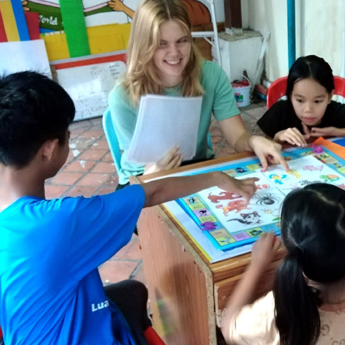 A young British woman and several Lao children play an English-learning board game