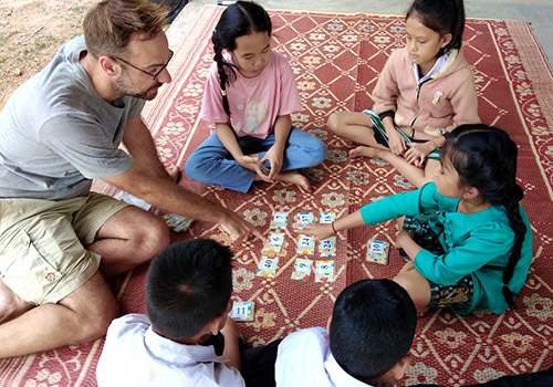 Lao children and a visitor play Mouse Math, in which they try to make equations from 9 cards on display.