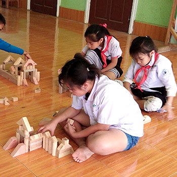 A small girl at Big Sister Mouse school in Laos, plays with wooden blocks.