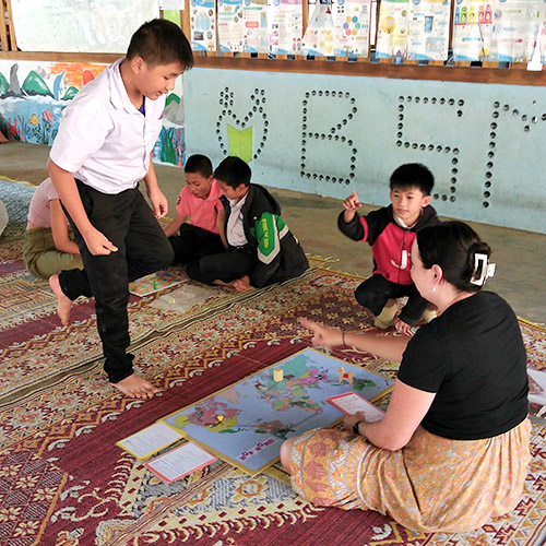 A Lao boy hops on one foot, while playing an English-learning game with a foreign visitor