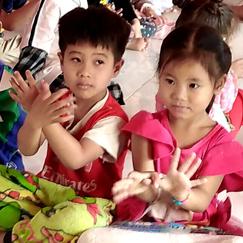 Two small Lao children learning to say 'butterfly' in Lao sign language