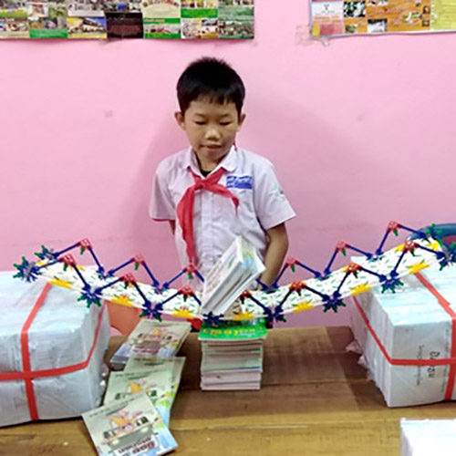 A boy tests the weight limit of a toy bridge made with K'Nex; it is breaking, under the weight of some books