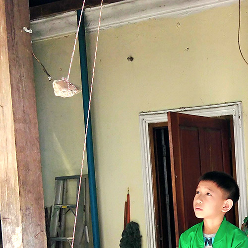 A boy watches a rock swing on a string, as part of a science experiment about pendulums