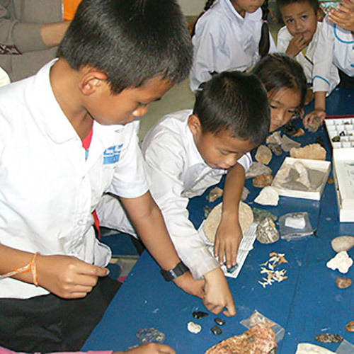 Several children inspect small rock and mineral specimens, and some fossilized shark teeth