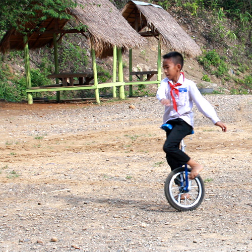 A boy riding a unicycle on a dirt lot