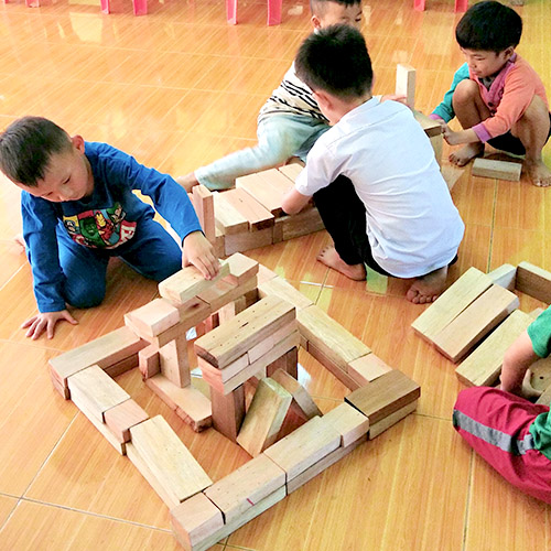 Preschool children play on the floor with wooden blocks.