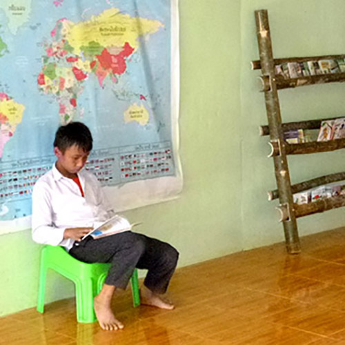 A boy reads a book as he waits to be picked up from Big Sister Mouse school in Luang Prabang, Laos,