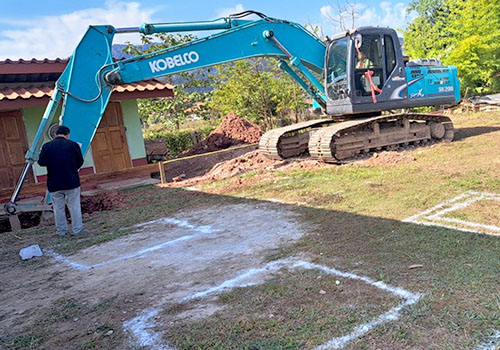 A digger (excavator) beginning to dig holes for a school foundation in Laos.