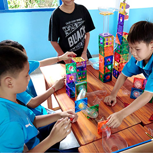 Children play with magnetic tiles and a ball that rolls through tunnels