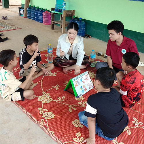 Children and teachers sit on floor, looking at pictures, and using sign language