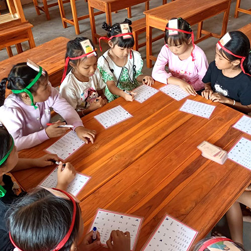 Schoolchildren in Laos sitting around a table with cards on their forehead.