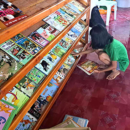 A girl looks through books on the shelves of Little Elephant preschool in Bokeo, Laos