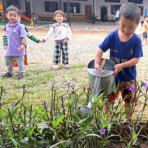A small boy waters flowers in garden at Little Elephant preschool in Laos