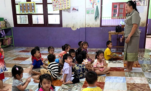 Small children play on floor, a teacher supervises