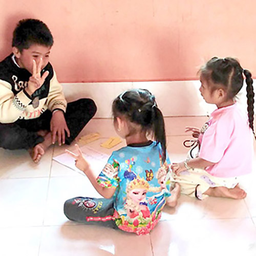 A boy teaches Lao sign language to two small girls at Little Rabbit school, Udom Xai, Laos