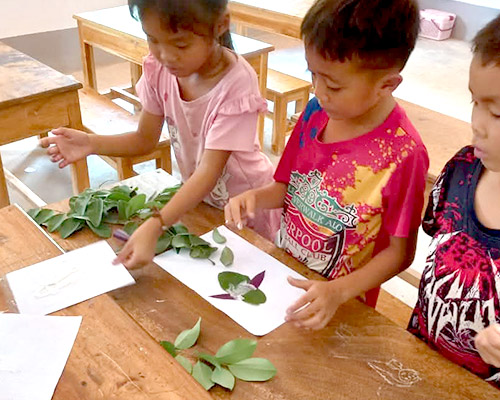 Children make art by gluing leaves to paper
