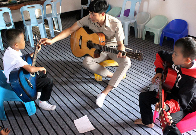 A teacher and two children play guitar together at Ton Kit school in Laos