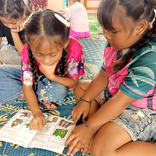 A young girl helps another learn to read