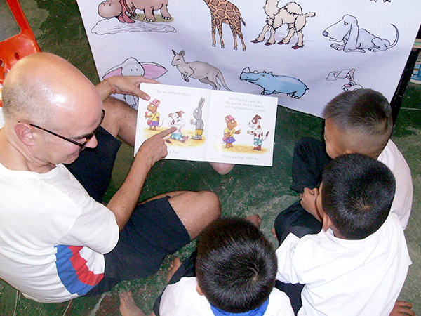 A visitor to Laos looks at a poster with animal pictures, with Lao students, practicing English together