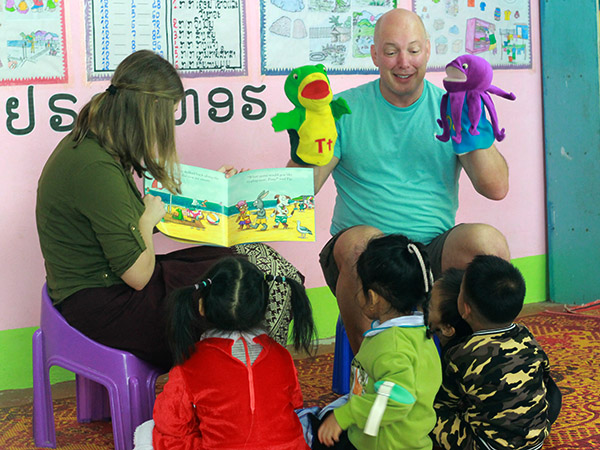 A man holds up two puppets while talking to children