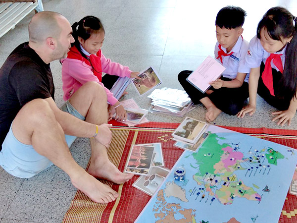 A man and four Laotian children  sit on school floor with map, playing a geography game