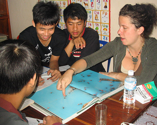 A visitor looks at an atlas with three young Lao students.