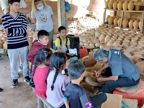 A pottery shop in Laos: Two adults and five children watch the potter at work.